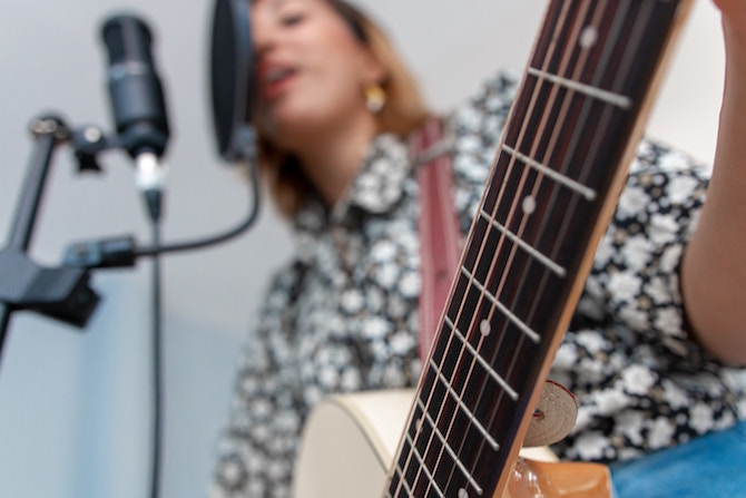 Girl singing in microphone while she plays guitar