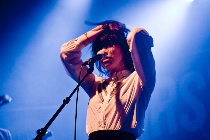 Woman in blue light performing on stage in front of a microphone