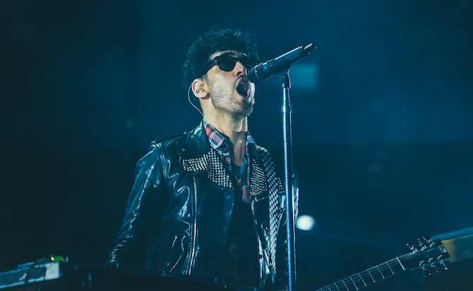 Joven con gafas de sol cantando en un micrófono en el escenario con luces azules