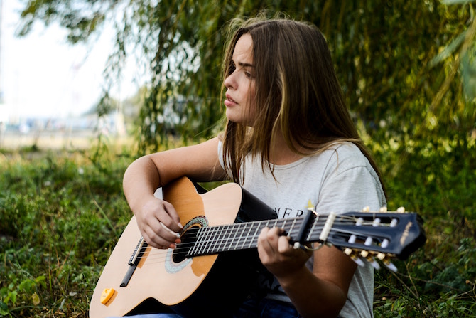 A young woman playing guitar and singing in a field