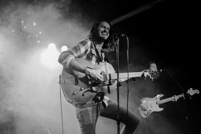 Man playing guitar on stage singing strongly into a microphone