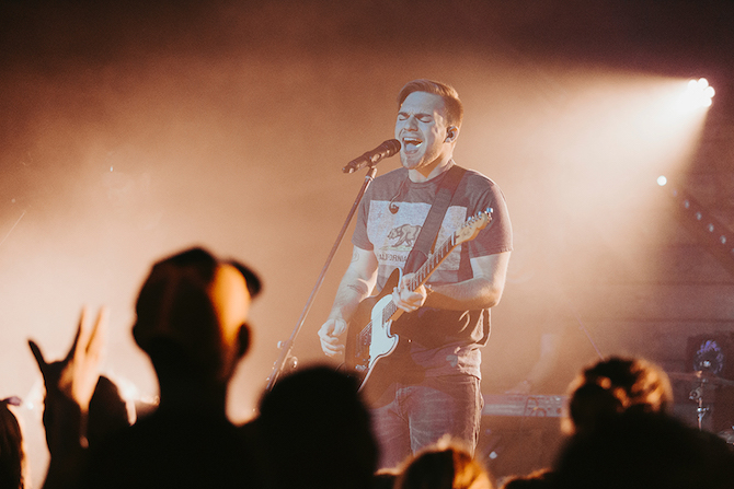 A guitarist sings open-mouthed on a microphone