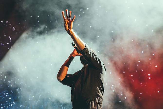 Young man at a concerting singing into a microphone holding 4 fingers up