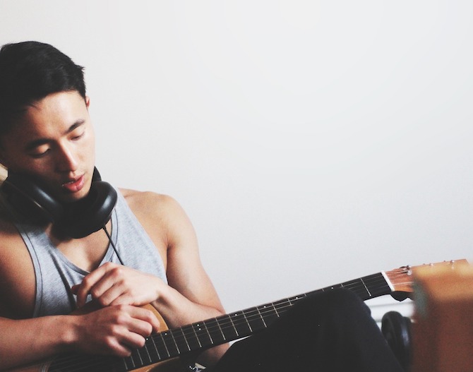 young asian man with guitar and headphones against a white background